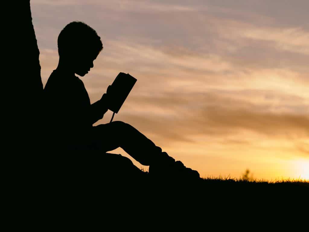 Child sitting in the sunset reading.