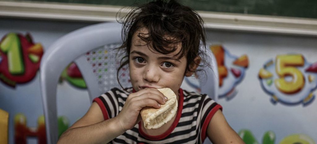 En ung pige spiser brød, der er blevet uddelt af World Food Programme på en UNRWA-skole i Gaza.