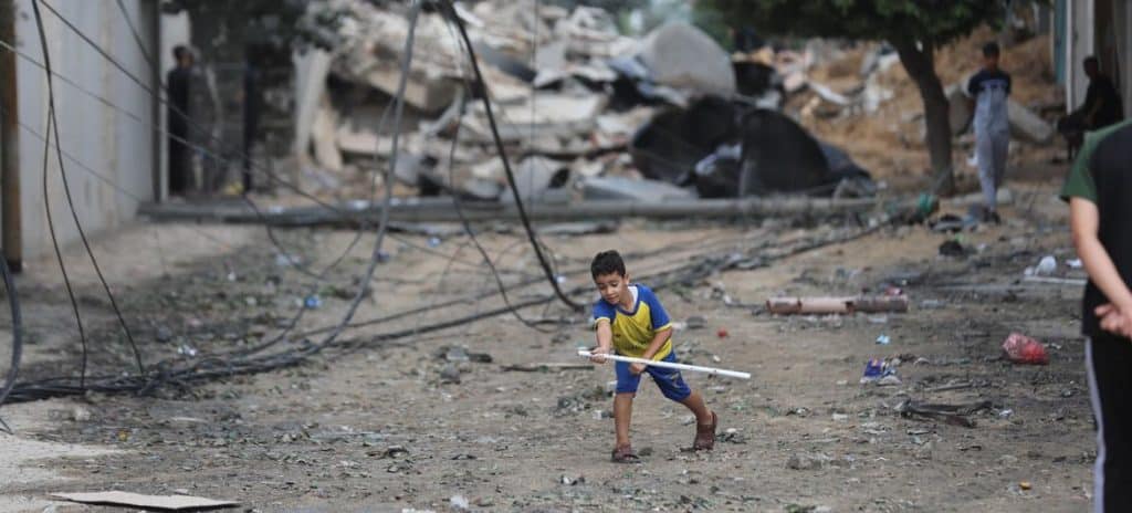 En ung dreng leger på gaden midt i ødelæggelserne af hjem, der er blevet ødelagt af luftangreb i Al Shati-flygtningelejren.
