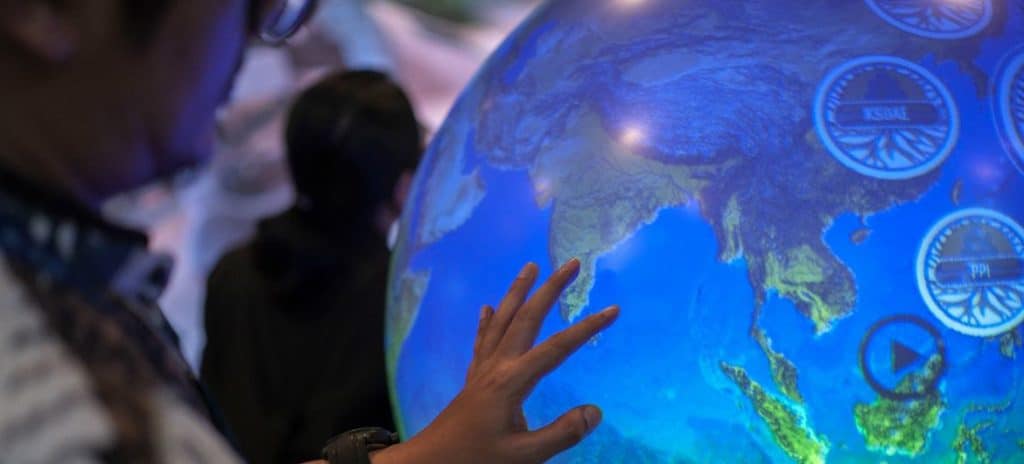 Billede af en hånd der rører en stor lysende globus til COP28