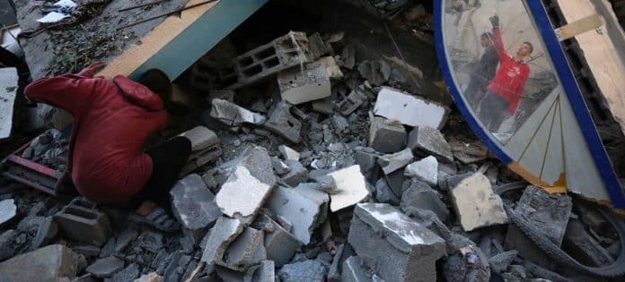 BIlledet viser en person der leder efter sine genstande i en bunke af murbrukker fra bombningen af Gaza