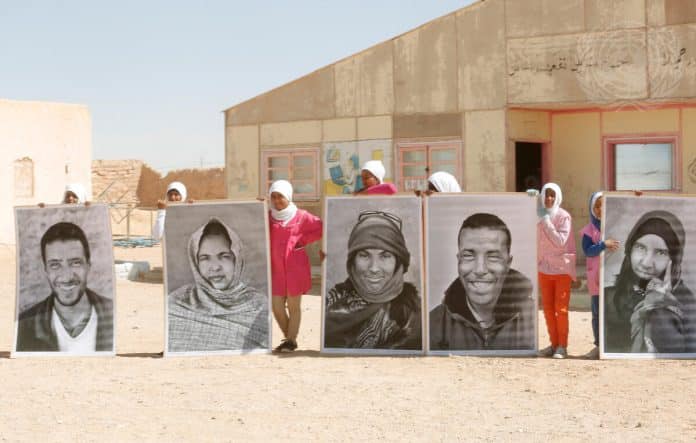 En gruppe saharawiske flygtninge holder store portrætter op under FN's generalsekretærs besøg i Smara-flygtningelejren uden for Tindouf i Algeriet i 2016. FN Foto/Evan Schneider