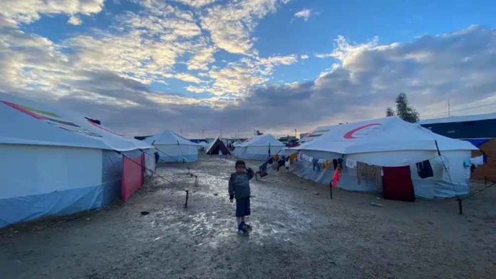 Child stands outside tents in Gaza.