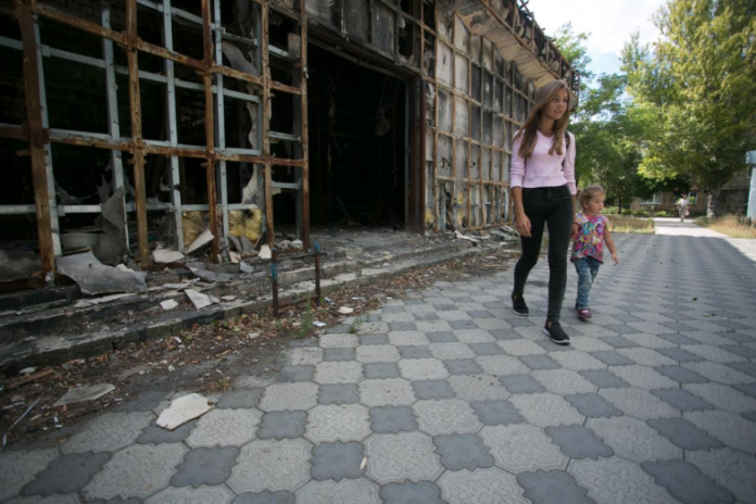 Woman and child walking next to bombed building