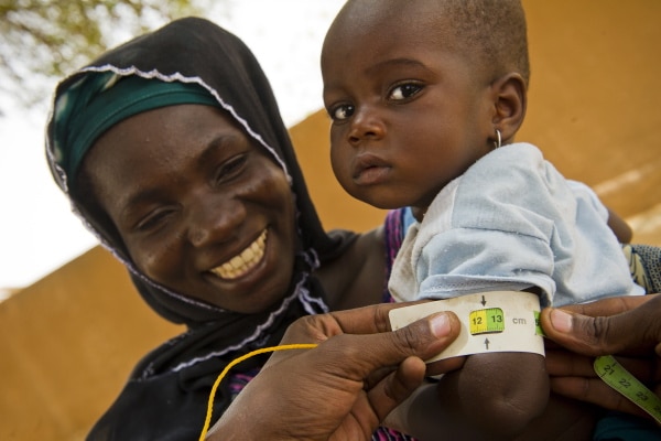Femme nigérienne tenant dans les bras son enfant. Il porte un bracelet montrant qu'il est sorti de la malnutrition