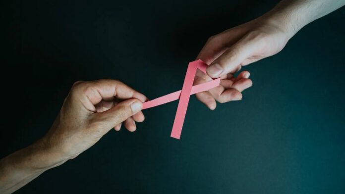 deux mains tiennent un ruban rose contre le cancer