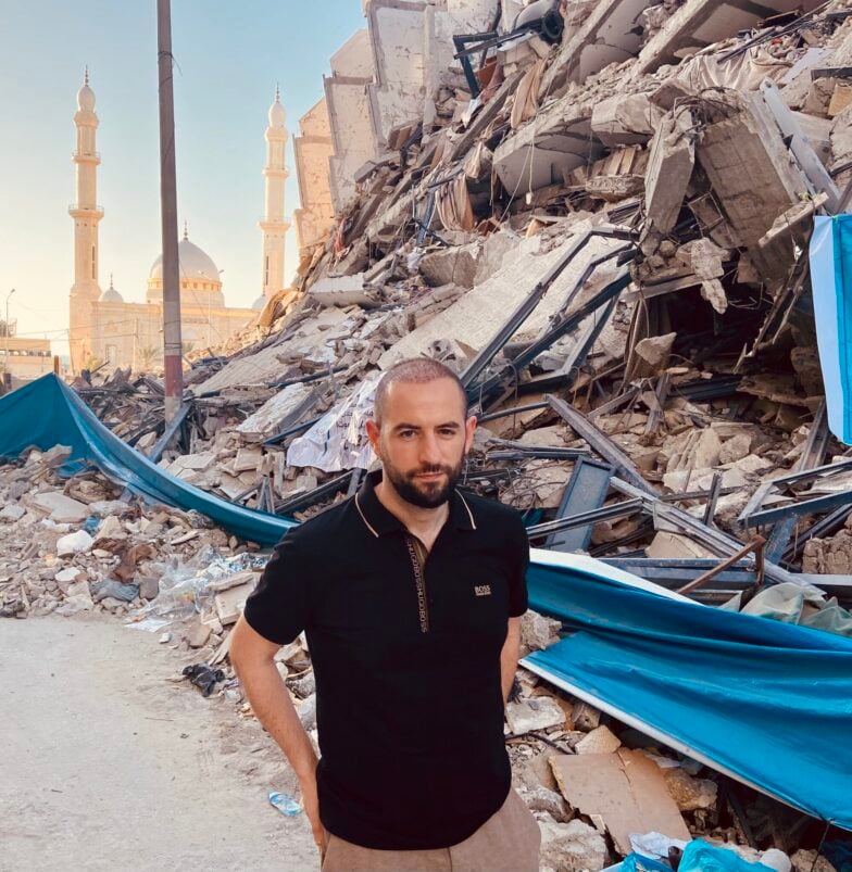Johan Soufi dans les rues de Gaza avec un immeuble détruit en arrière plan