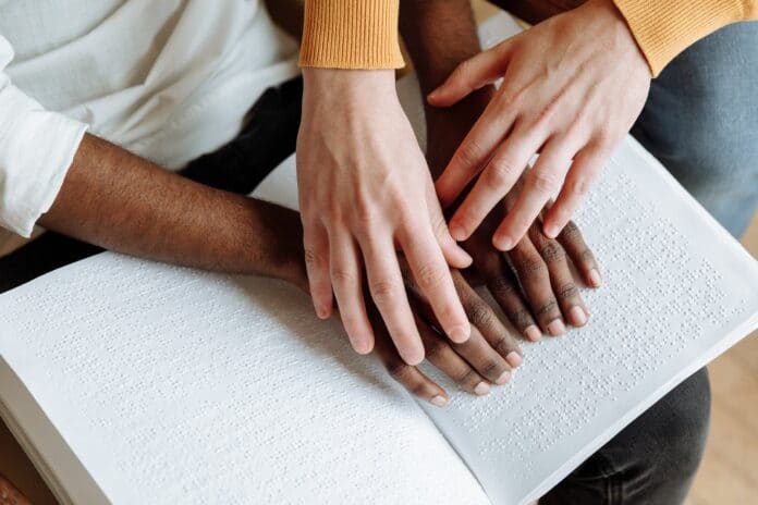 Personnes handicapées - Les mains de deux personnes l’une aidant l’autre à lire le braille