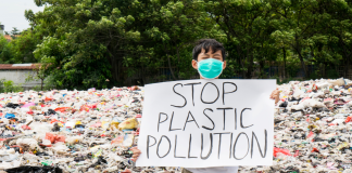 Enfant tenant une pancarte stop à la pollution plastique sur une plage pleine de plastique