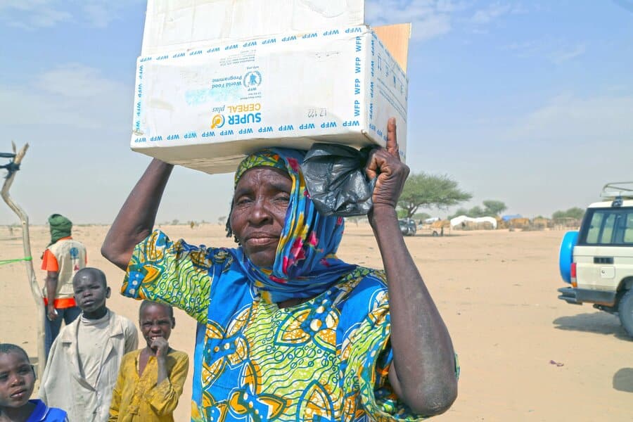 femme sahelienne portant un carton d'aide alimentaire sur la tête