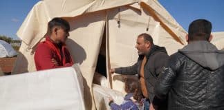 Des victimes rescapées du séisme devant une tente blanche recevant de l'aide humanitaire, en l'occurence des matelas.