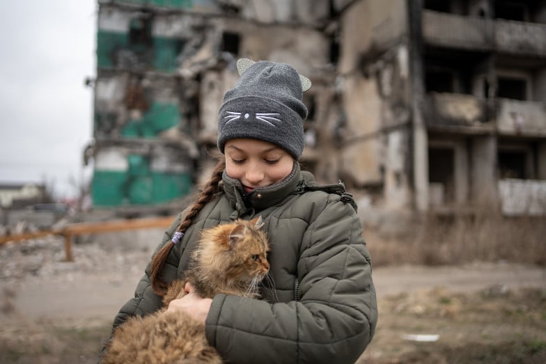 fille qui tient un chat devant un bâtiment détruit en Ukraine