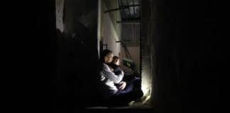 Man houdt zijn zoontje 's nachts vast in hun huis de Gazastrook, afgebeeld in foto.
