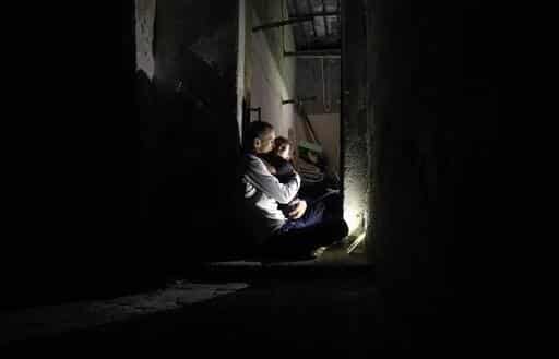Man houdt zijn zoontje 's nachts vast in hun huis de Gazastrook, afgebeeld in foto.