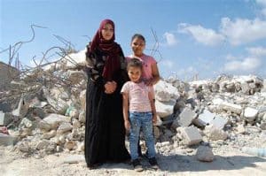 Mom Med 2 barn med bombet hus i bakgrunnen