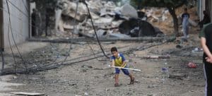 en gutt som leker alene mellom bombede byggninger