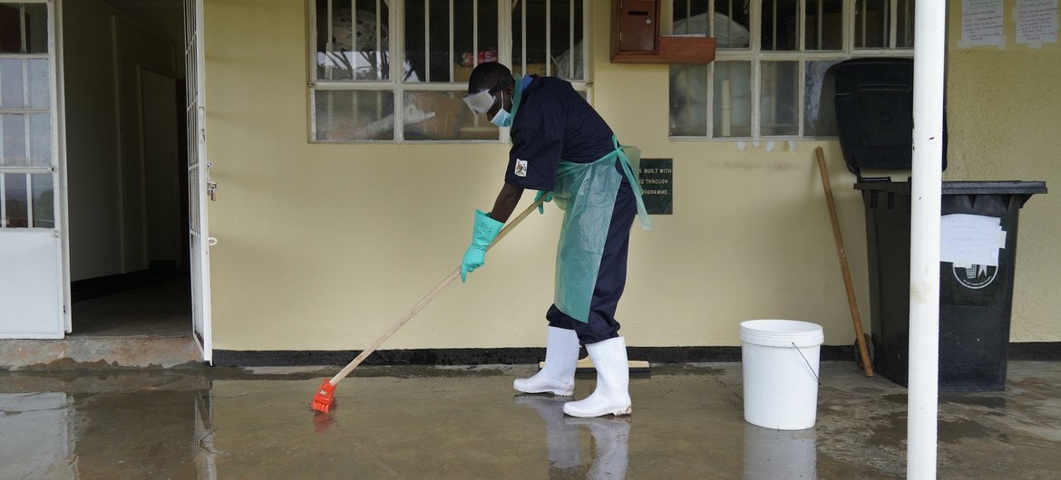 Funcionário de um centro de saúde em Uganda limpa o chão usando uma mistura de cloro e água para prevenir infecções. Serviços adequados de água, saneamento e higiene nas instalações de saúde são vitais para proteger as populações contra infecções.