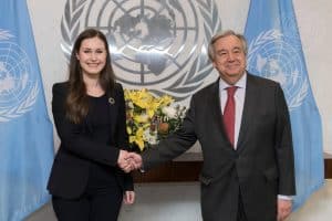 Sanna Marin och Antonio Guterres skakar hand framför FN-flaggan