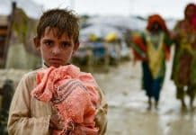 Ett barn med ett föremål i handen i förgrunden, fuktig mark i bakgrunden.