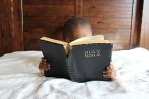 En pojke som sitter i en säng med Bibeln uppslagen framför sig