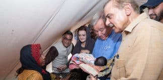 Fyra människor som samlats kring en baby i en primitiv miljö. Babyn hålls av Antonio Guterres.