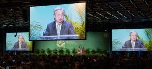 FNs generalsekreterare Guterres på en skärm i konferensmiljö