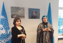 Två kvinnor som står bredvid varandra flankerade av två av FNs flaggor.