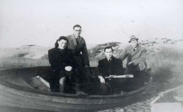 ett svartvitt foto av tre män och en kvinna till sjöss i en mindre träbåt.