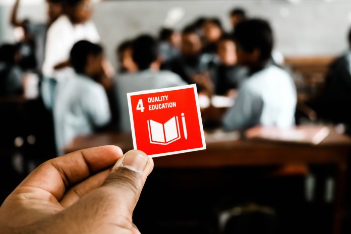 En skolklass i bakgrunden och en hand som håller upp en röd ruta med texten education