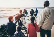 En man och tre barn som håller varandra i hand framför en strand