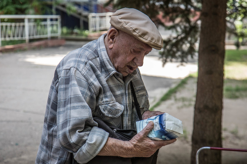 Äldre man på gatan som tittar på ett paket livsmedel. 