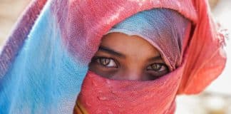 En kvinna med slöja i närbild, man ser hennes ögon mellan färgglada tygstycken.