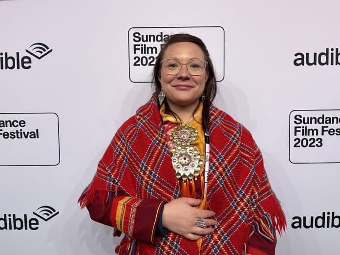 En kvinna med traditionell samisk klädsel står mot en vägg