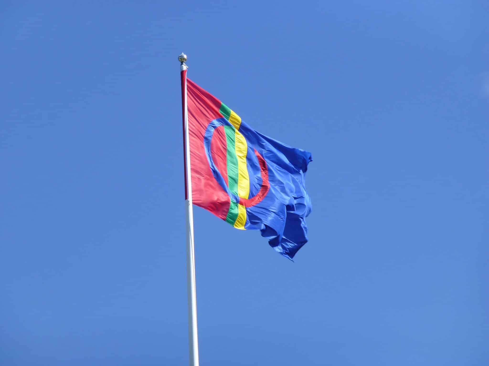 En bild på den vajande samiska flaggan i färgerna blå, röd, grön och gul