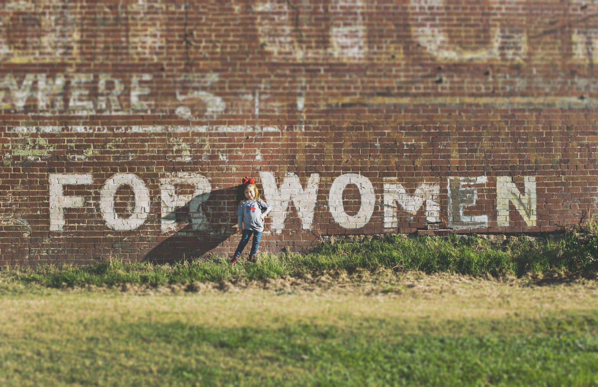 En flicka som står mot en vägg där det står FOR WOMEN