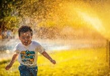 En liten pojke som springer i en vattenspridare och ser glad ut