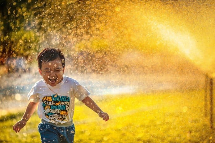 En liten pojke som springer i en vattenspridare och ser glad ut