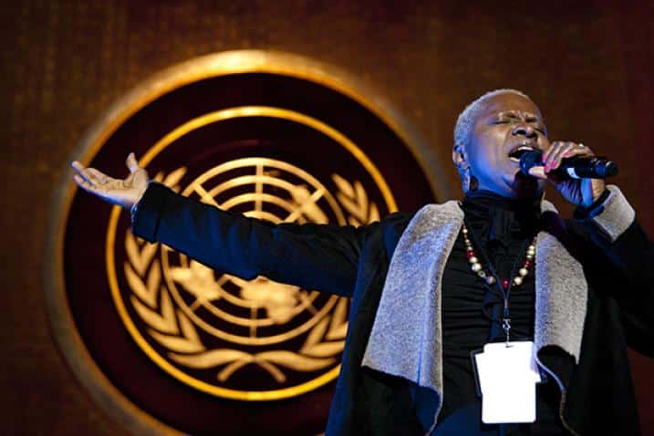 En kvinna som sjunger i en mikrofon och FNs logo i bakgrunden. 