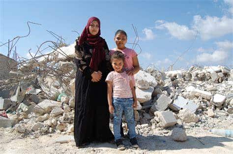 En mamma och två barn som står i en stadsmiljö i ruiner