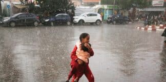 Ett barn som bär ett mindre barn i famnen i ösregn