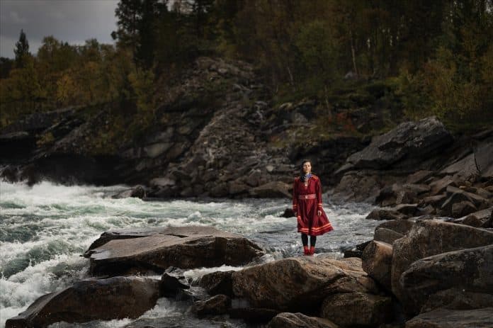 En kvinna i samisk klädsel som står vid vatten.
