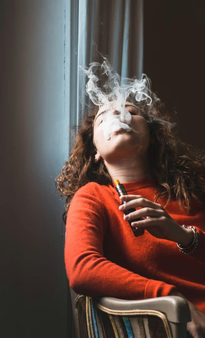 En kvinna som röker en e-cigarett, delvis täckt av rök
