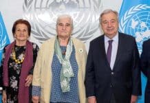 Fyra människor som står på rad med FN flaggan i bakgrunden