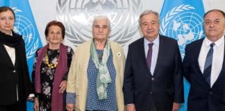 Fyra människor som står på rad med FN flaggan i bakgrunden